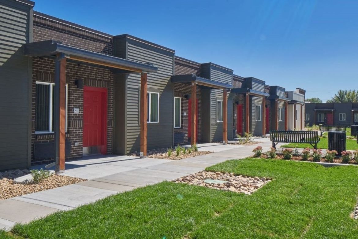 Exterior view of VWC3, row home style units made up of dark brown brick and dark green siding, red doors with awnings